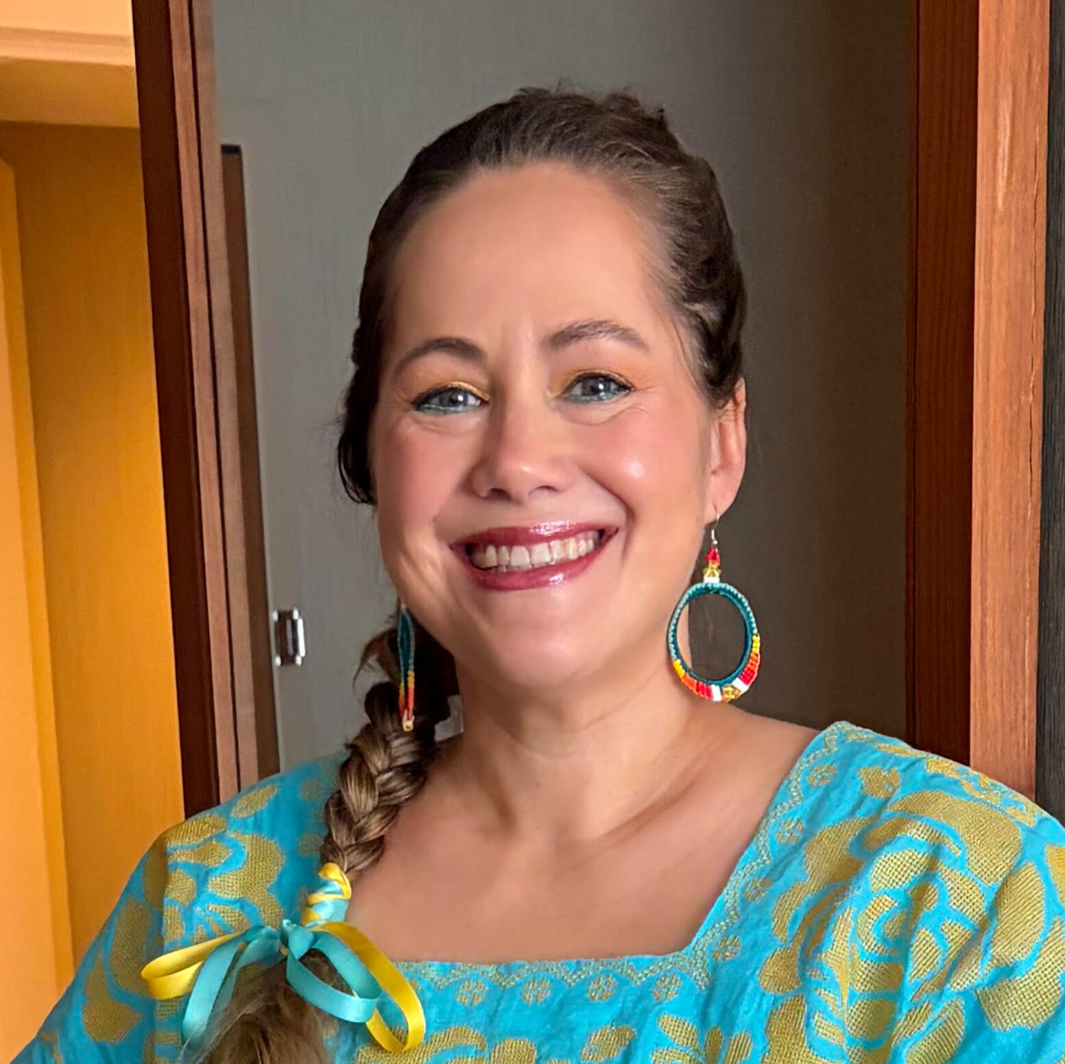 Author thumbnail author with single braid with yellow and blue ribbons and beaded hoop earrings